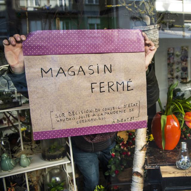 Un fleuriste pose une affiche pour annoncer la fermeture temporaire de son magasin de fleurs suite a la fermeture des magasins dans le canton de Vaud le lundi 16 mars 2020 a Lausanne. Le gouvernement vaudois a decide lundi de prendre de nouvelles mesures exceptionnelles pour proteger la population contre le coronavirus (Covid-19). L'arrete interdit l'exploitation des lieux de commerce, sauf les commerces d'alimentation ou de premiere necessite. [KEYSTONE - Jean-Christophe Bott]