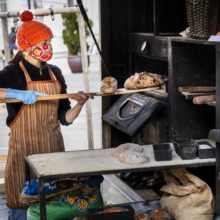 Une marchande prépare du pain sur un stand pendant la crise de Coronavirus à La Chaux-de-Fonds. [Keystone - Jean-Christophe Bott]
