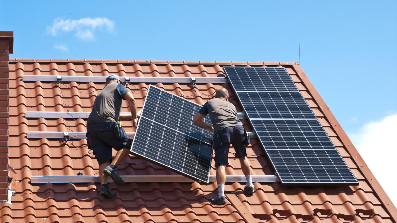 Deux ouvriers installent des panneaux solaires sur le toit d'une maison. [Depositphotos - AHatmaker]