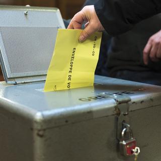 Une personne dépose son enveloppe de vote avec son bulletin de vote a l'intérieur dans une urne. [Keystone - Gabriel Monnet]