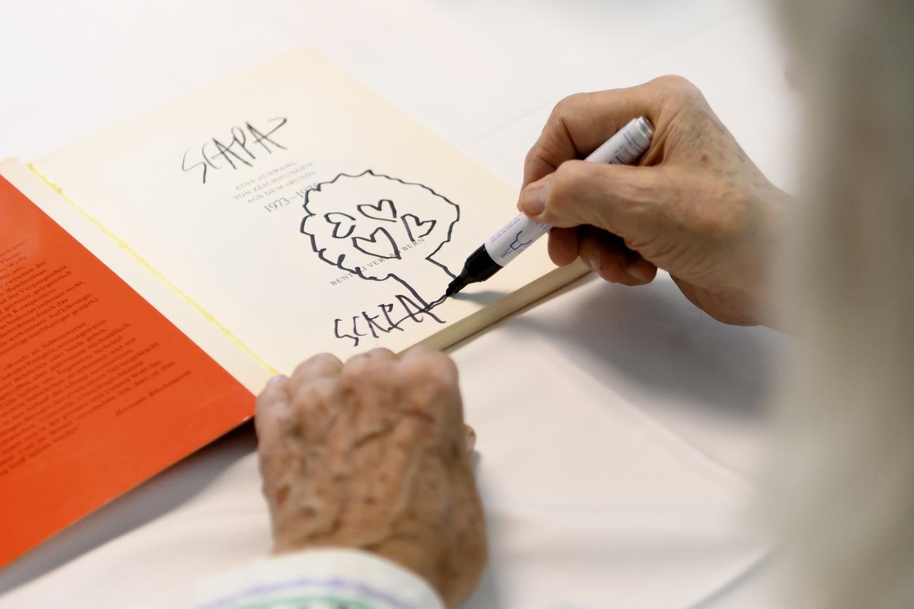 L'artiste suisse Ted Scapa dédicace un livre lors du vernissage de la nouvelle exposition de Scapa intitulée "MUSIQUE ? VIN ? GOLF", le jeudi 1er juillet 2021, au Burgerspittel dans le quartier de Viererfeld, à Berne. [Keystone - Anthony Anex]