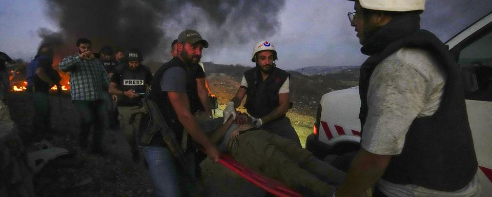 Des employés de la Défense civile transportent Elie Brakhya, caméraman de la télévision qatarie d'Al-Jazeera, qui a été blessé par les bombardements israéliens, dans le village frontalier d'Alma al-Shaab avec Israël, au sud du Liban, le vendredi 13 octobre 2023. [Keystone - Hassan Amar]