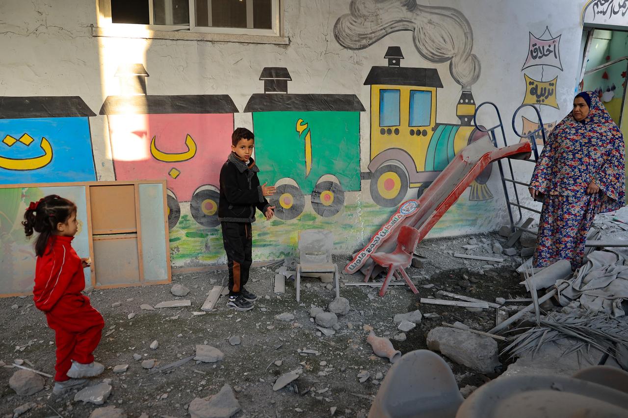 Une femme et des enfants se tiennent au milieu des décombres d'un jardin d'enfants touché par les bombardements israéliens à Rafah, dans le sud de la bande de Gaza, le 9 décembre 2023. [AFP - Saïd Khatib]