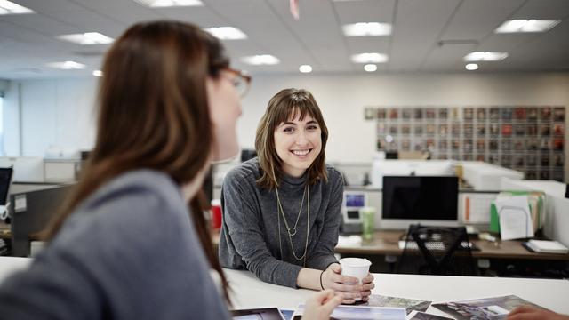 Deux femmes assises dans un bureau discutent et rient (image d'illustration). [Mint Images via AFP - MINT IMAGES]