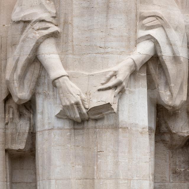 Des mains tiennent une bible sur la sculpture de Jean Calvin sur le Mur de la Réforme, à Genève. [Keystone - Gaetan Bally]