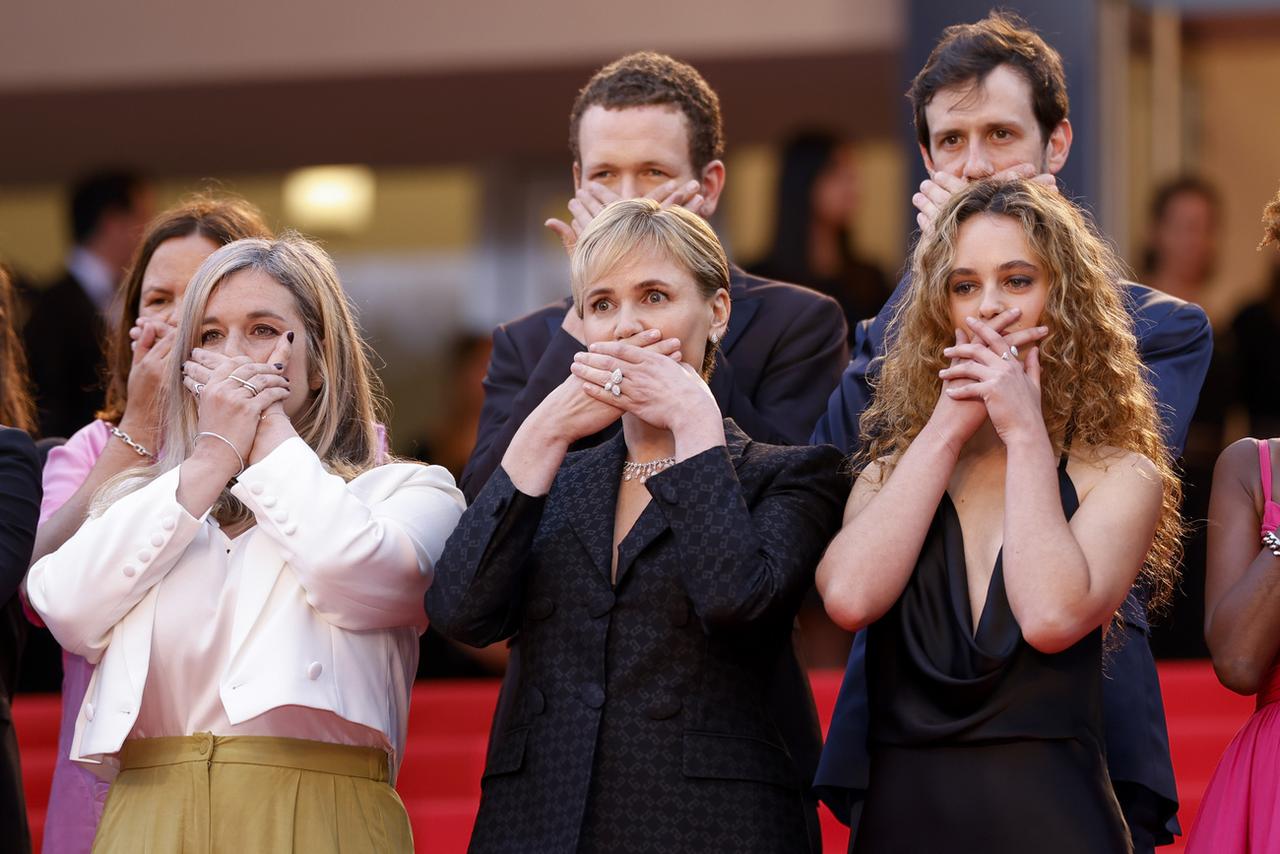 Judith Godrèche, réalisatrice du court métrage "Moi aussi" (au centre) et les membres de son équipe, sur les marches, ont croisé leurs mains devant leur bouche, symbole du silence imposé aux victimes de violences sexuelles. [KEYSTONE - VIANNEY LE CAER]