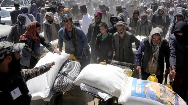 Un combattant taliban monte la garde alors que des personnes reçoivent des rations alimentaires distribuées par un groupe d'aide humanitaire chinois, pendant le mois sacré du Ramadan, à Kaboul, en Afghanistan, samedi 30 avril 2022. [Keystone]