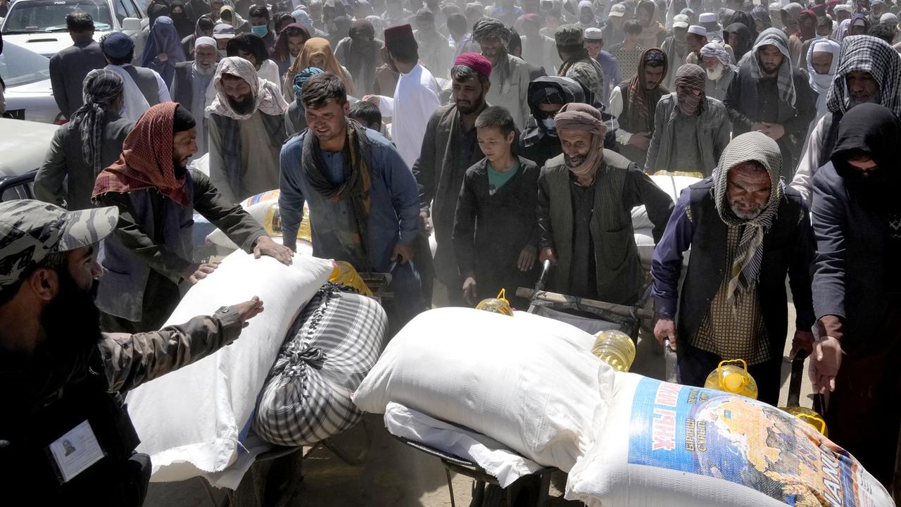 Un combattant taliban monte la garde alors que des personnes reçoivent des rations alimentaires distribuées par un groupe d'aide humanitaire chinois, pendant le mois sacré du Ramadan, à Kaboul, en Afghanistan, samedi 30 avril 2022. [Keystone]