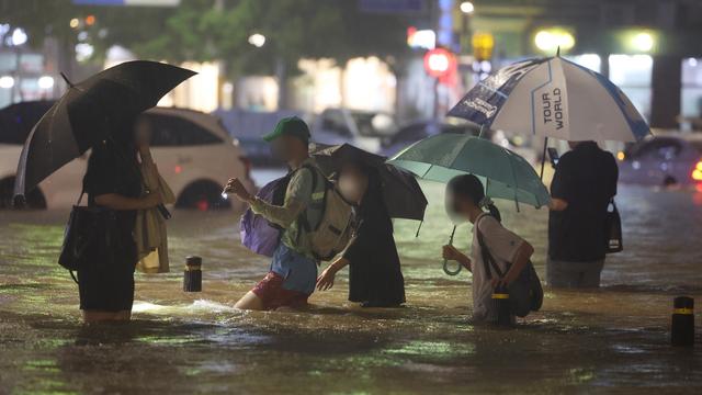 Des passants traversent une routes inondée à Séoul alors que des pluies diluviennes ont commencé lundi en Corée du Sud [KEYSTONE]