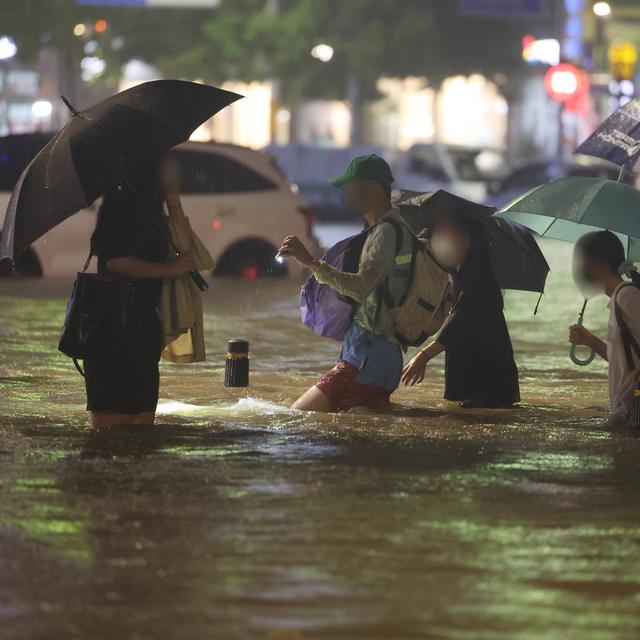 Des passants traversent une routes inondée à Séoul alors que des pluies diluviennes ont commencé lundi en Corée du Sud [KEYSTONE]