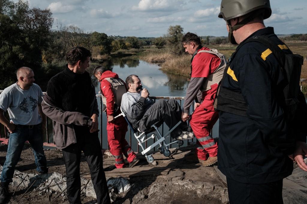 Un homme est transporté sur une chaise roulante alors qu'il traverse le pont détruit sur la rivière Oskil lors de son évacuation de la rive orientale récemment reprise par les forces ukrainiennes à Kupiansk, dans la région de Kharkiv, le 29 septembre 2022. [AFP - YASUYOSHI CHIBA]