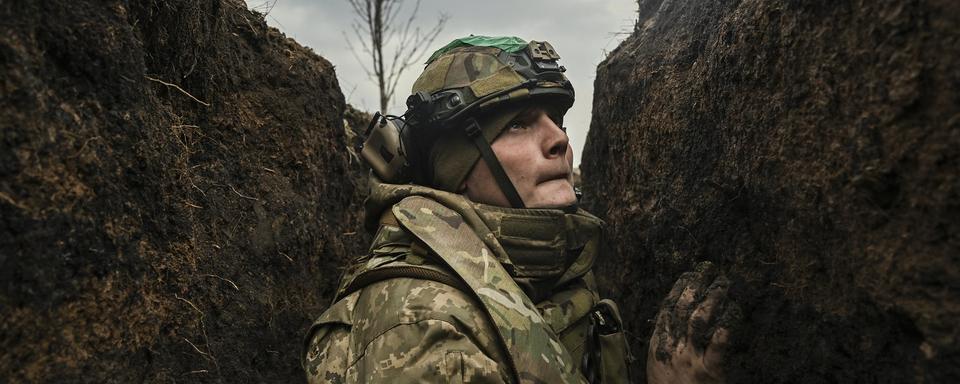 Le 8 mars 2023, un soldat ukrainien s'abrite dans une tranchée près de la ville de Bakhmout lors d'un bombardement. Plus d'un an après le lancement de l'"opération militaire" russe en Ukraine, le conflit s'enlise. [AFP - Aris Messinis]