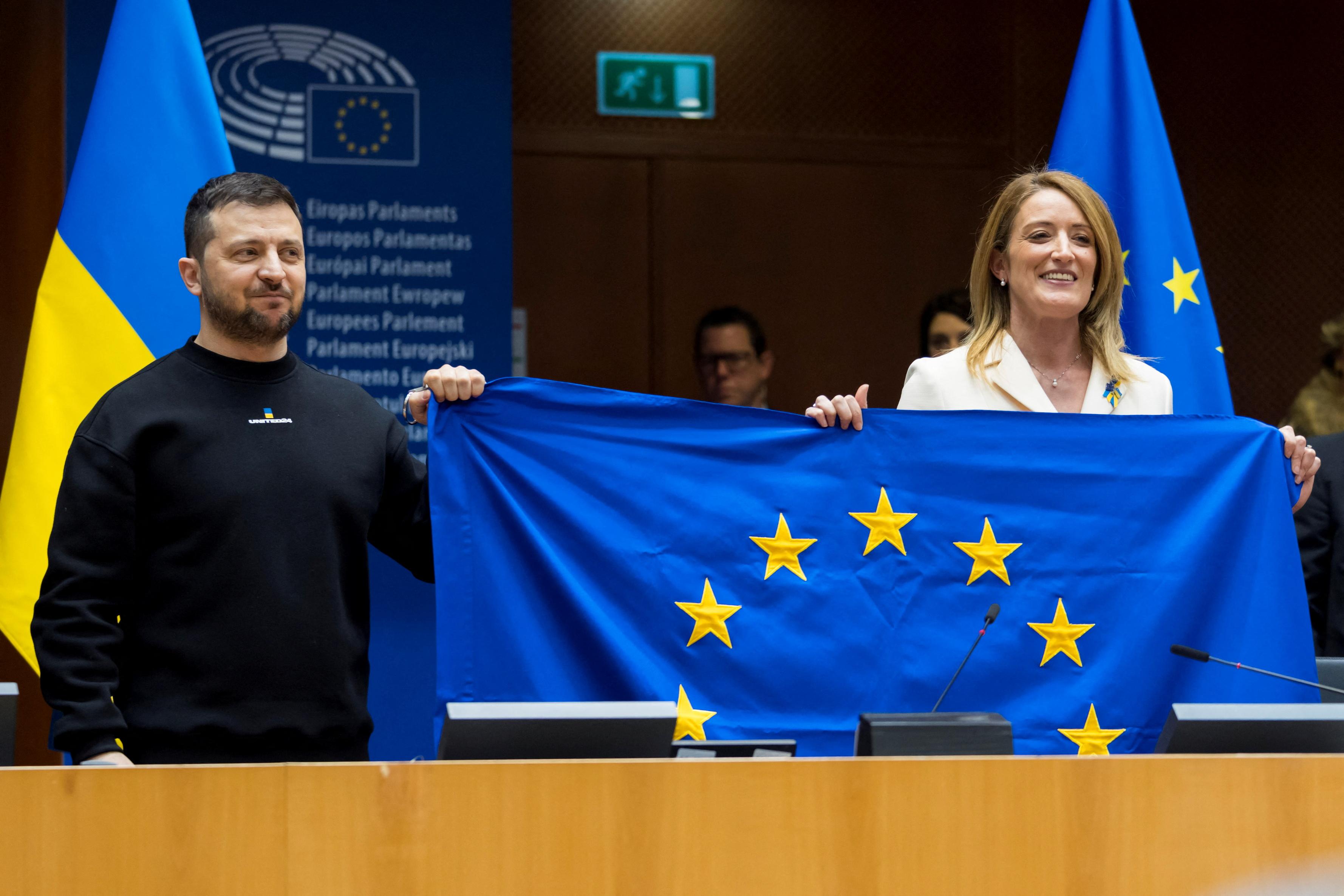 La présidente du Parlement européen Roberta Metsola et le président ukrainien Volodymyr Zelensky tiennent un drapeau de l'UE lors de la visite de ce dernier à Bruxelles, le 9 février 2023. Des négociations d'adhésion ont été annoncées le 14 décembre, mais le chemin est encore long avant que l'Ukraine ne rejoigne les 27. [REuters - Daina Le Lardic/Union européenne]