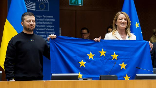 La présidente du Parlement européen Roberta Metsola et le président ukrainien Volodymyr Zelensky tiennent un drapeau de l'UE lors de la visite de ce dernier à Bruxelles, le 9 février 2023. Des négociations d'adhésion ont été annoncées le 14 décembre, mais le chemin est encore long avant que l'Ukraine ne rejoigne les 27. [REuters - Daina Le Lardic/Union européenne]