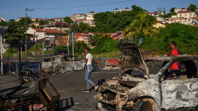 Des piétons passent derrière une voiture brûlée suite aux récentes manifestations sur le coût de la vie, à Fort-de-France, Martinique, le 23 septembre 2024. [AFP - ED JONES]