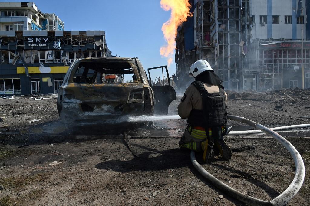 Un pompier se tient devant un centre commercial de Kharkiv, détruit de dimanche par une frappe russe. [AFP - SERGEY BOBOK]