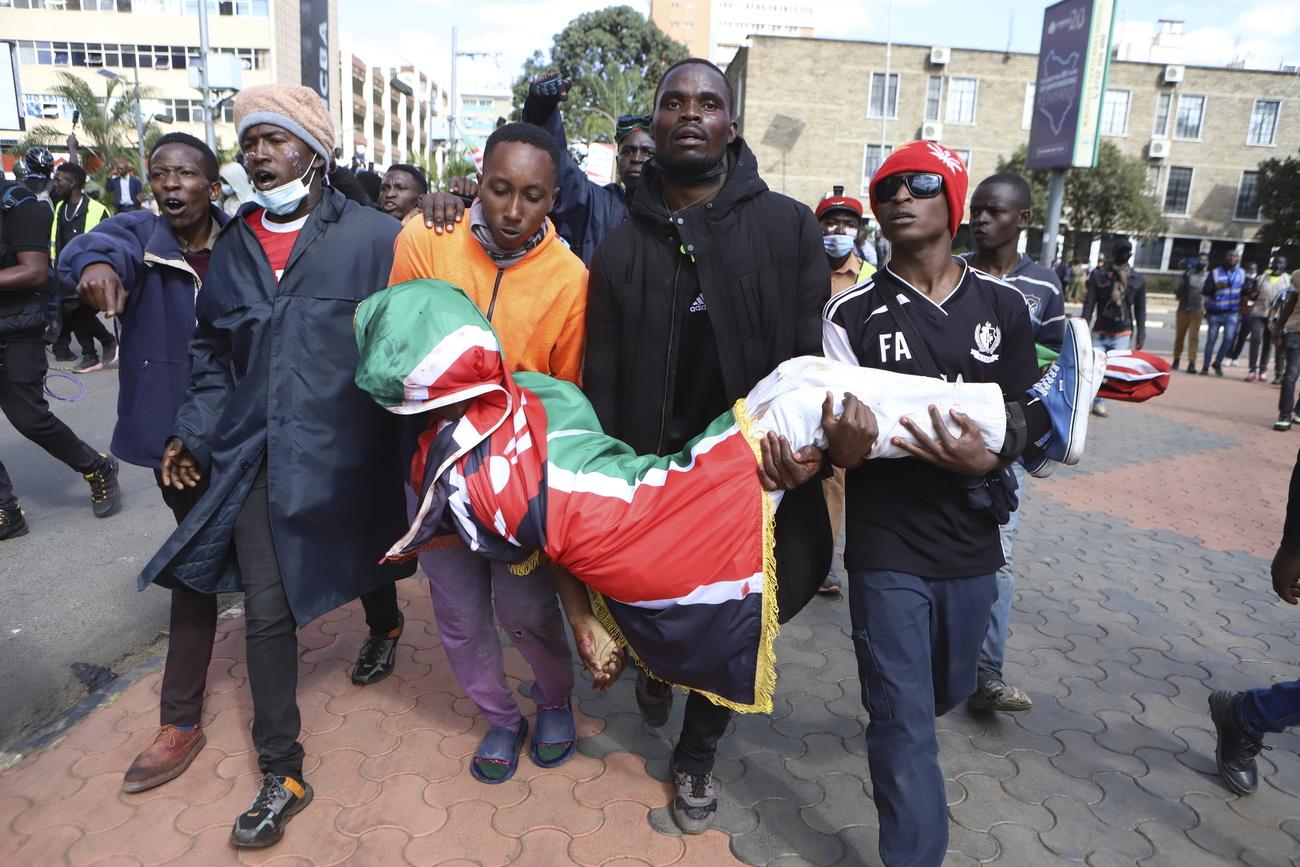 Des hommes portent le corps d'un manifestant visé par balle lors d'une violente manifestation, à Nairobi, au Kenya, le 25 juin. [KEYSTONE - ANDREW KASUKU]