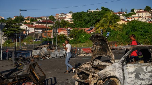 Des piétons passent derrière une voiture brûlée suite aux récentes manifestations sur le coût de la vie, à Fort-de-France, Martinique, le 23 septembre 2024. [AFP - ED JONES]