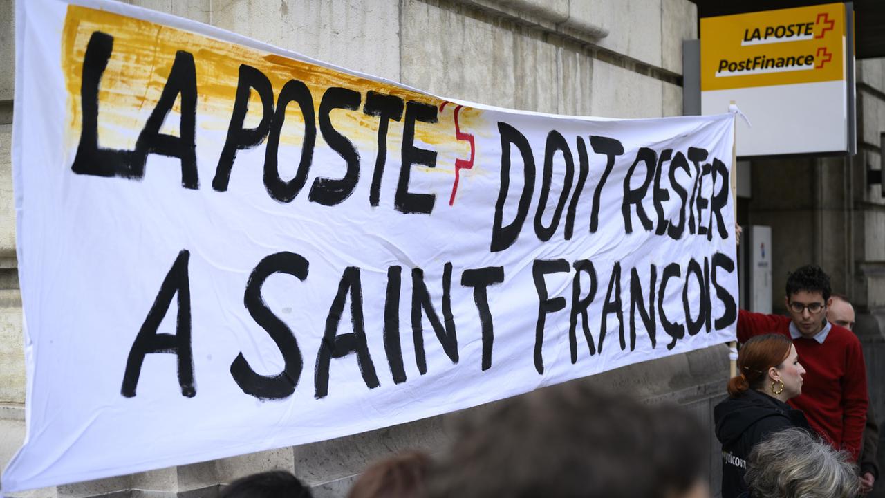 Les membres d'un comité pour le maintien de La Poste tiennent une banderole "La Poste doit rester a Saint-François", le jeudi 23 mars 2023 à Lausanne. [Keystone - Laurent Gillieron]