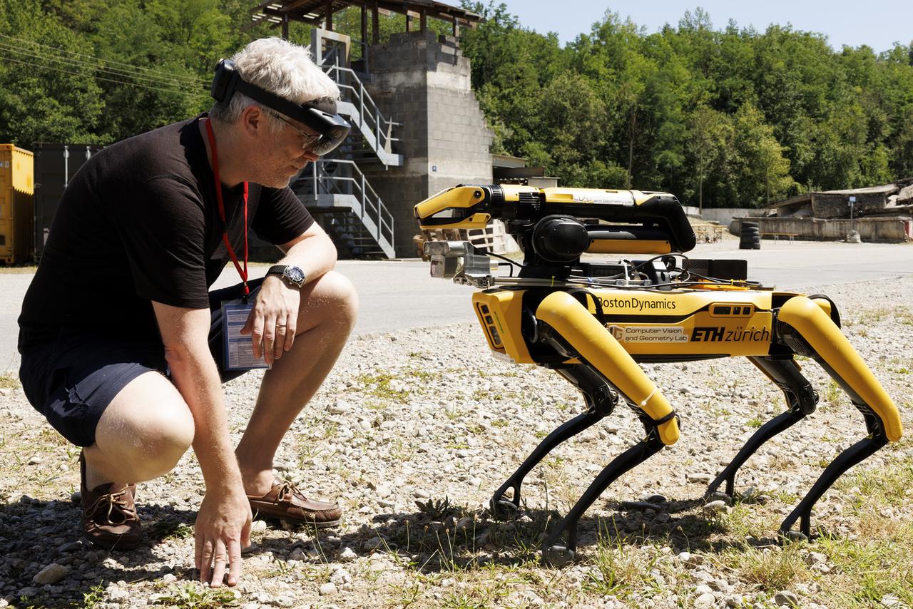 Marc Pollefeys, professeur d'informatique à l'École polytechnique fédérale de Zurich et directeur du laboratoire de réalité mixte et d'IA de Microsoft à Zurich, portant des lunettes de réalité mixte, pose à côté de Spot, le robot à quatre pattes, lors de la conférence ARCHE 2023. [Keystone - Salvatore Di Nolfi]