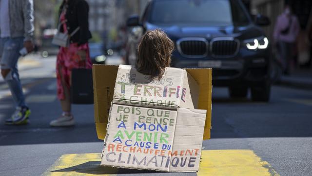 Un militant d'Extinction Rebellion (XR) assis sur la route face à une voiture à Genève. [Keystone - Salvatore Di Nolfi]