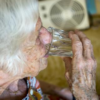 Une personne âgée s'hydrate pour se prévenir des fortes chaleurs. [Image d'illustration] [Keystone - Jean-Christophe Bott]
