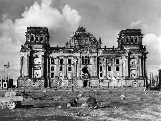 Devant le bâtiment détruit du Reichstag en 1946, deux personnes déterrent une souche d'arbre afin d'en faire un combustible. [Keystone - Photoèress-Archiv]