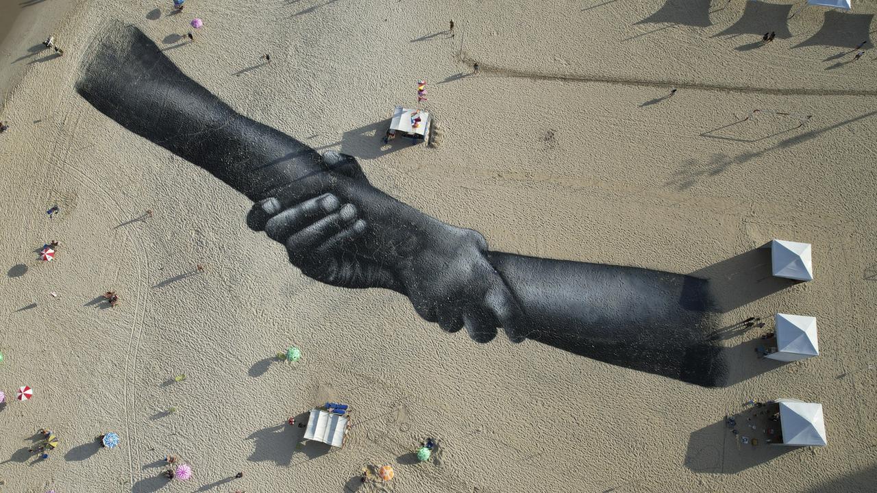 La Suisse doit "combler ses lacunes" en matière de protection des droits humains. (Sur la photo, une fresque de land art réalisée avec de la peinture biodégradable par l'artiste franco-suisse Saype, couvre la plage de Copacabana à Rio de Janeiro, au Brésil, le vendredi 15 juillet 2022). [Keystone - Silvia Izquierdo]