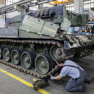 Un mécanicien entretient les chenilles d'un char de type Leopard 2 dans une halle de maintenance de RUAG, le 20 mars 2023, à Thoune. [Keystone - Peter Schneider]