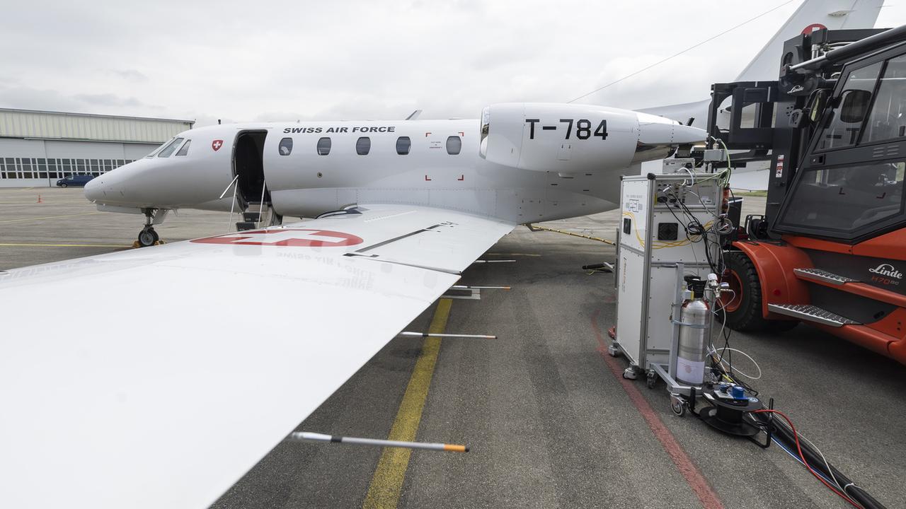 Un avion de la Swiss Air Force au sol est connecté a des machines qui analysent les émissions du moteur lors du test d'un nouveau carburant d'aviation durable, le 24 mai 2023 a l'aérodrome militaire de Payerne. [Keystone - Cyril Zingaro]