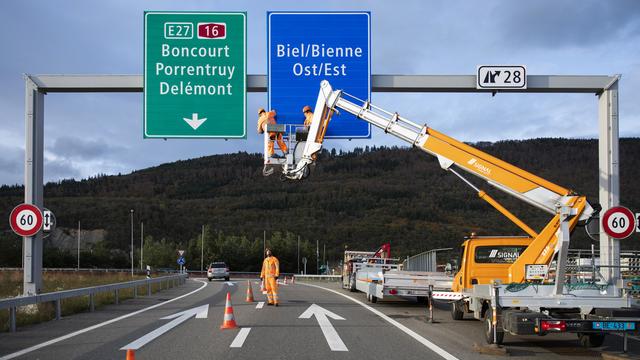 Des travailleurs installent un panneau bilingue "Biel/Bienne" sur l'autoroute à Bienne. [KEYSTONE - PETER KLAUNZER]