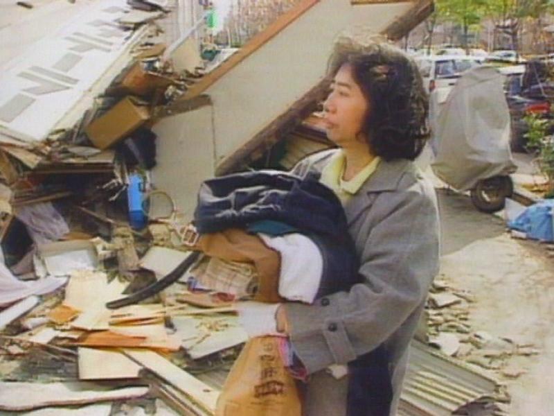 Une rescapée devant les débris de sa maison après le séisme à Kobe en 1995. [RTS]