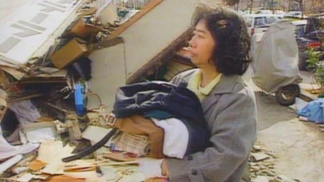 Une rescapée devant les débris de sa maison après le séisme à Kobe en 1995. [RTS]