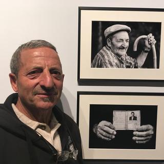 Rocco, habitant du Trièves d’origine italienne posant à côté de photographies de son père au Musée dauphinois [RTS - Christophe Canut]