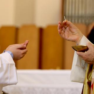 Main de l'évêque qui dispense la Sainte Eucharistie pendant la communion. [Depositphotos - ChiccoDodiFC]