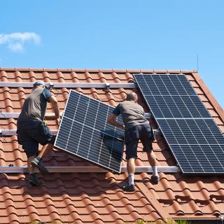 Deux ouvriers installent des panneaux solaires sur le toit d'une maison. [Depositphotos - AHatmaker]