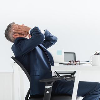 Un employé de bureau / homme d'affaires prend son visage dans ses mains, épuisé à son bureau. [Depositphotos - AndrewLozovyi]