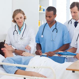 Une personne allongée dans un lit d'hôpital discute avec une équipe médicale. [Depositphotos - Wavebreakmedia]