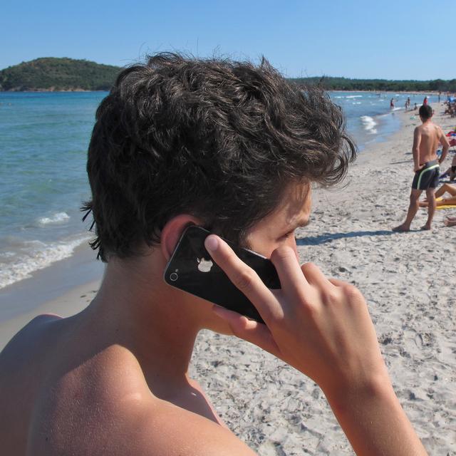 Un jeune au téléphone sur une plage en Corse.