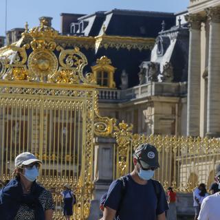 Des touristes portant un masque devant le Château de Versailles.