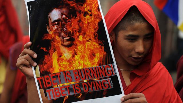 En Inde, dans un défilé de protestation en février 2012, un moine tibétain tient une affiche symbolisant l'immolation d'un religieux. [AFP - Diptendu Dutta]